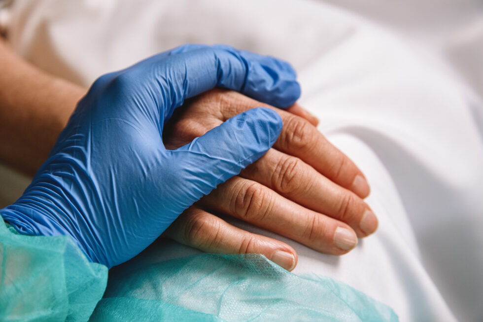 A nurse's gloved hand upon the top of a patient's hand.