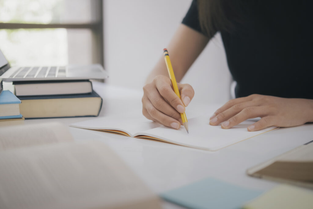 Photo of lady taking notes with a laptop and books nearby